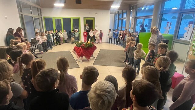 Die Schulfamilie steht im Kreis um den Adventskranz in der Aula