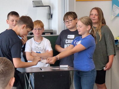 Eine Schülerin steht vor der Klasse und führt einen Kartenzaubertrick vor