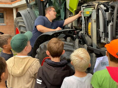 Schüler stehen vor einem Claas-Traktor mit geöffneter Motorhaube