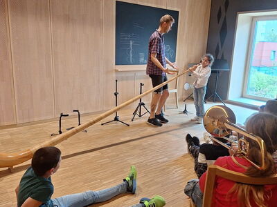 Schüler sitzen in einem Raum vor einem aufgebauten Alphorn