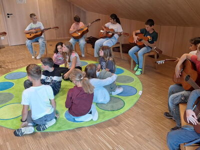 Schüler sitzen auf Stülen in einem Kreis und haben Klassikgitarren in der Hand