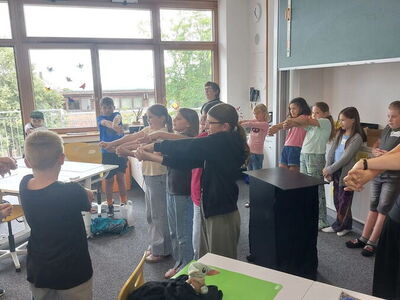 Die Schüler stehen mit ausgestreckten Armen im Klassenzimmer